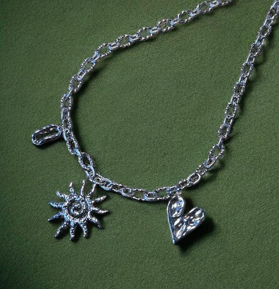 Bracelet à breloques argenté Elaia, posé sur un tissu vert