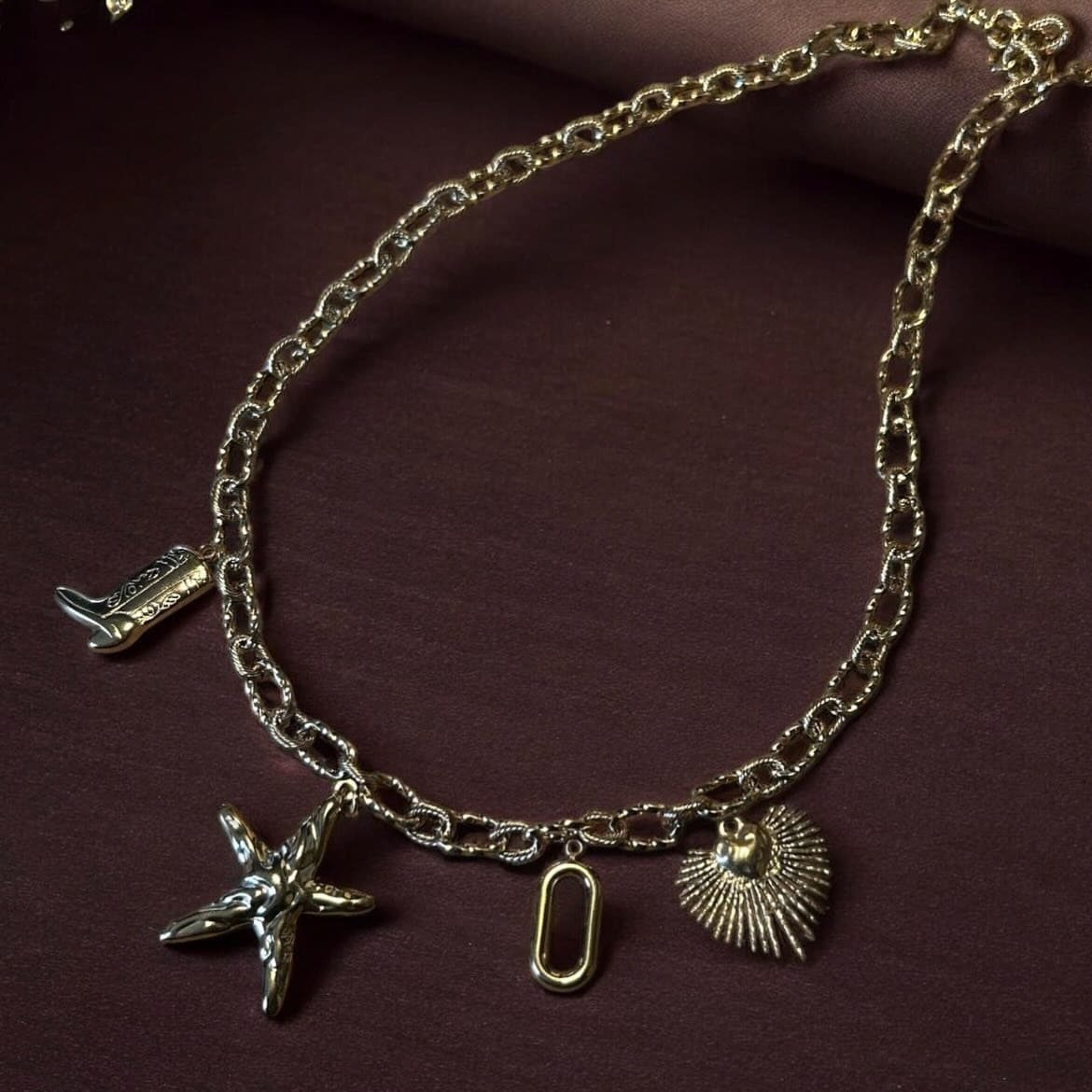 Bracelet à breloques doré Elaia, posé sur un tissu bordeaux